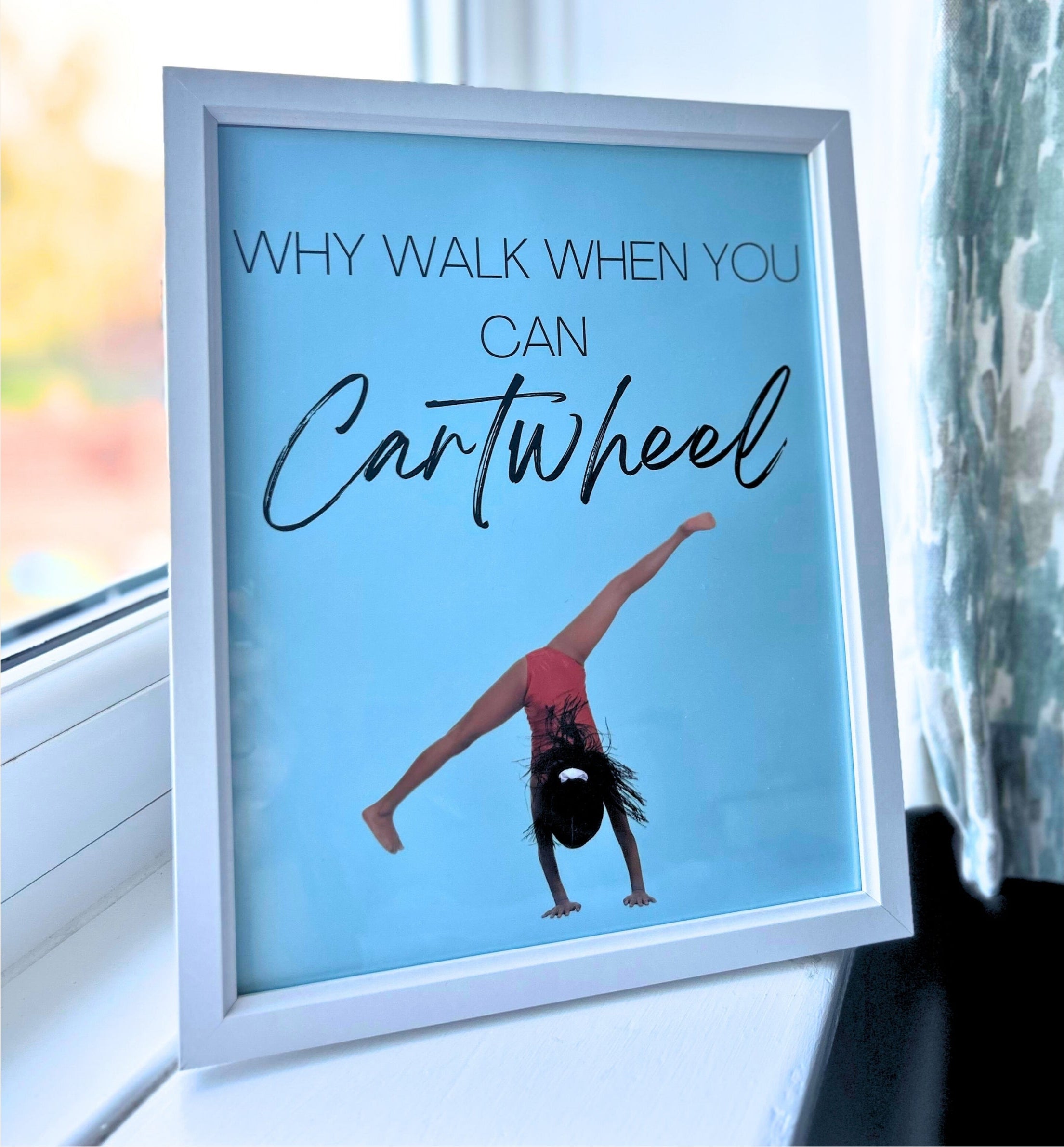 Framed gymnastics poster with a girl doing a cartwheel and text 'Why walk when you can cartwheel' on a blue background.