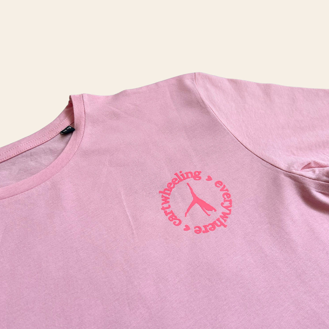 Pink gymnastics t-shirt with a cartwheel logo on a beige background