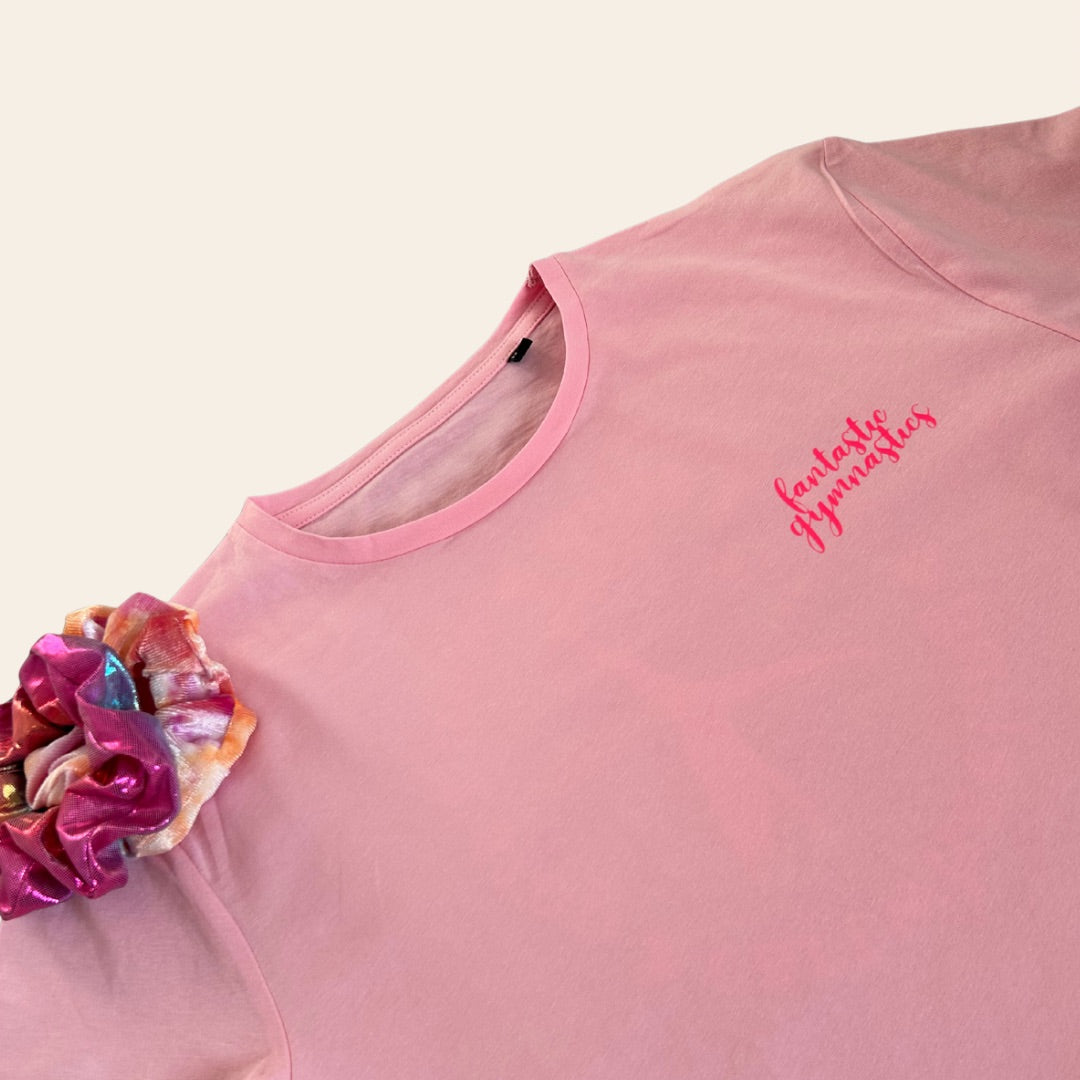 Pink gymnastics t-shirt with 'Fantastic Gymnastics' logo and colourful scrunchie on a beige background