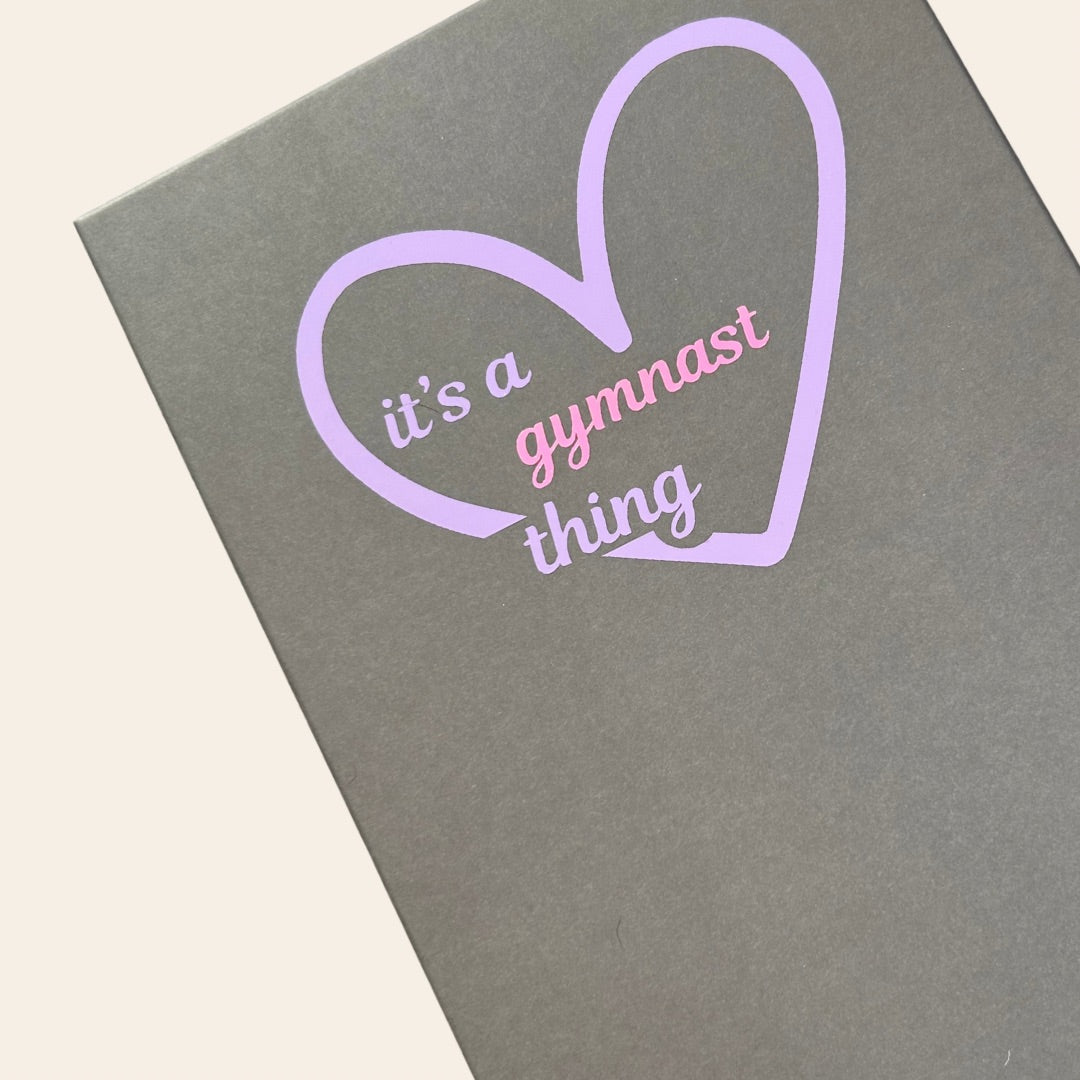 Grey A4 gymnastics certificate box with 'its a gymnast thing' and a heart on a beige background